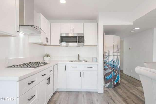 kitchen with wall chimney range hood, sink, stainless steel appliances, light hardwood / wood-style floors, and white cabinets