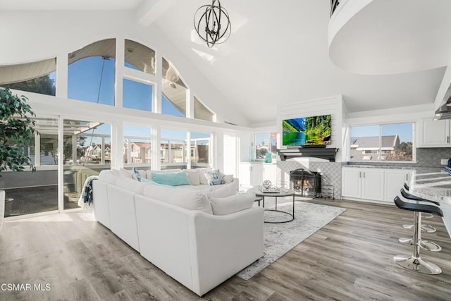 living room with beam ceiling, high vaulted ceiling, a chandelier, and light wood-type flooring