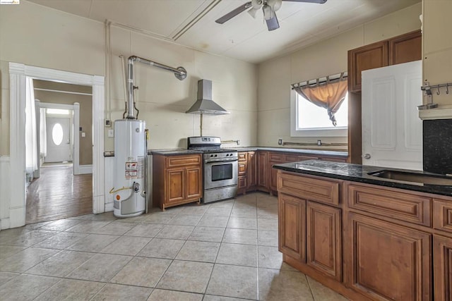 kitchen with ceiling fan, wall chimney exhaust hood, stainless steel range with gas cooktop, water heater, and light tile patterned floors