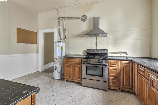 kitchen with wall chimney exhaust hood, stainless steel gas range, water heater, dark stone counters, and light tile patterned flooring