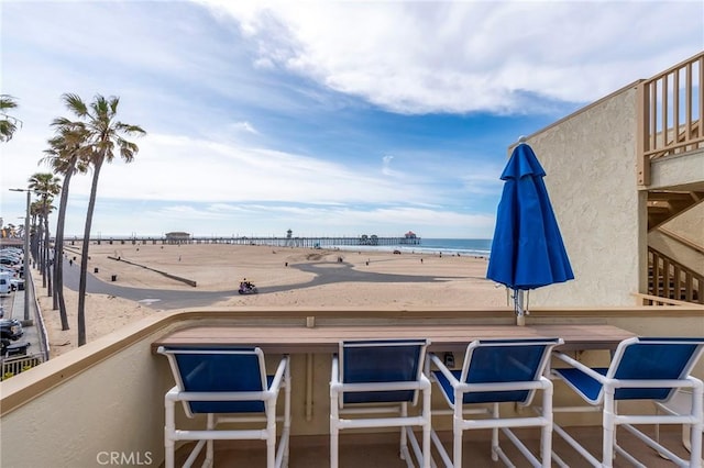 view of patio with a balcony, a bar, a water view, and a view of the beach