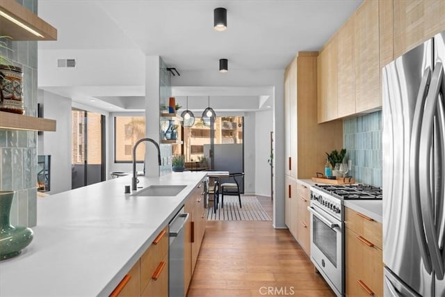 kitchen with tasteful backsplash, sink, stainless steel appliances, light brown cabinets, and light hardwood / wood-style flooring