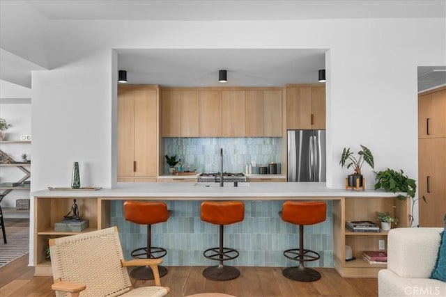 kitchen featuring light hardwood / wood-style flooring, stainless steel fridge, kitchen peninsula, and a kitchen bar