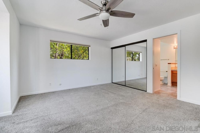 unfurnished bedroom featuring connected bathroom, light colored carpet, multiple windows, and ceiling fan