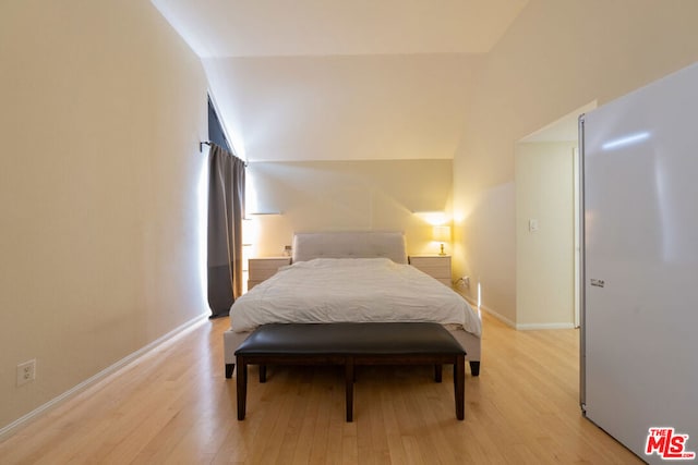 bedroom featuring stainless steel fridge, light wood-type flooring, and vaulted ceiling