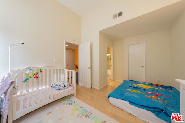 bedroom featuring wood-type flooring, a towering ceiling, and ensuite bathroom