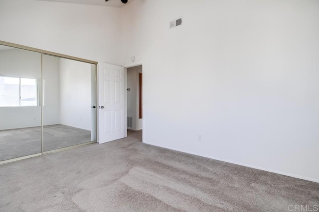 unfurnished bedroom featuring light carpet, high vaulted ceiling, and a closet