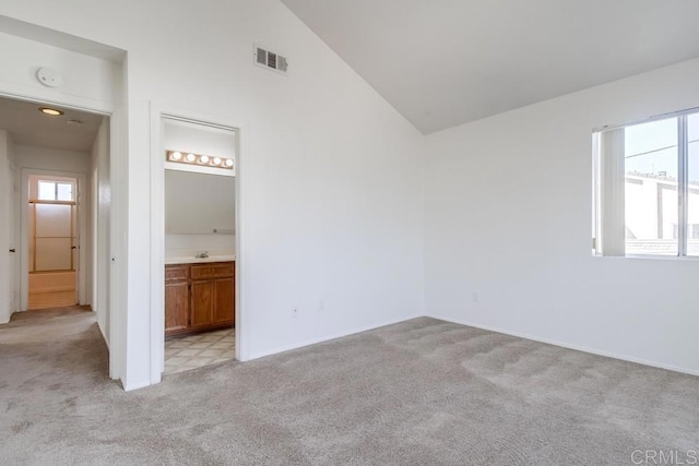 unfurnished bedroom with ensuite bathroom, lofted ceiling, and light carpet