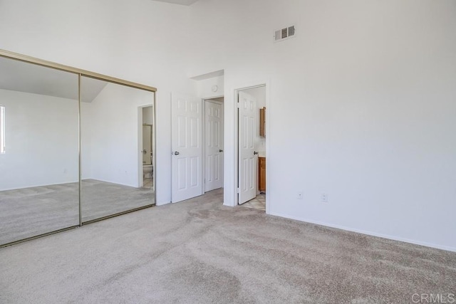 unfurnished bedroom with carpet floors, a towering ceiling, a closet, and ensuite bath