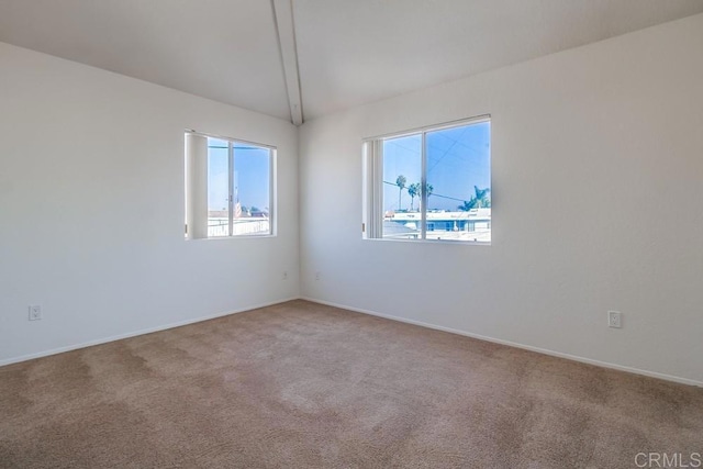 carpeted empty room featuring vaulted ceiling and baseboards