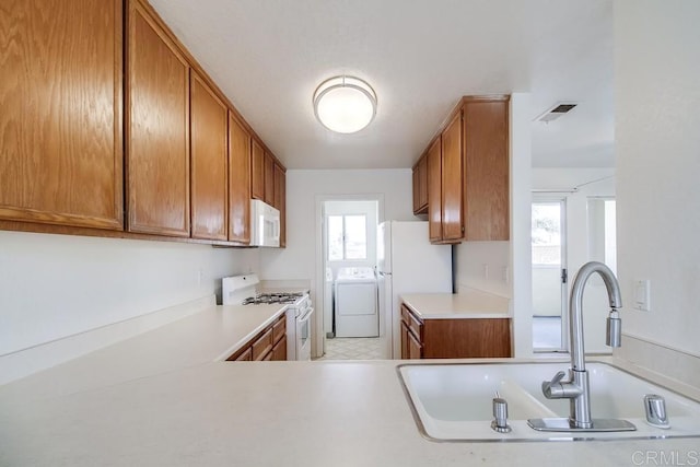 kitchen featuring white appliances, a sink, washing machine and dryer, and light countertops