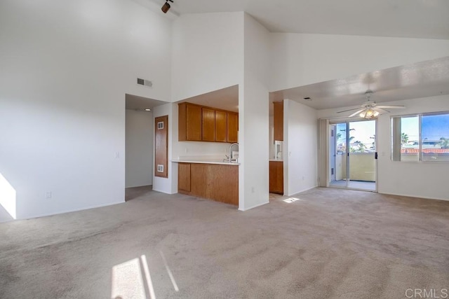 unfurnished living room with light colored carpet, high vaulted ceiling, a sink, a ceiling fan, and baseboards