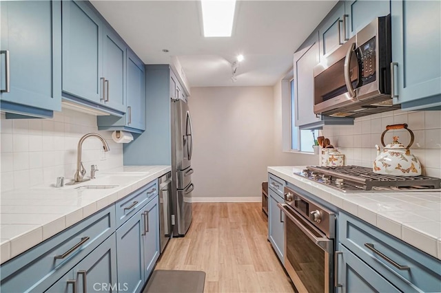 kitchen with light wood-type flooring, appliances with stainless steel finishes, sink, and blue cabinets