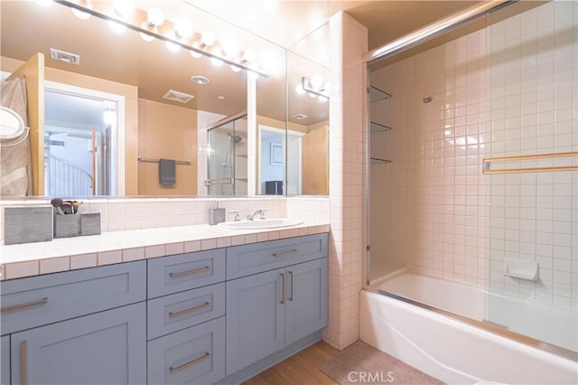 bathroom featuring combined bath / shower with glass door, decorative backsplash, hardwood / wood-style floors, and vanity