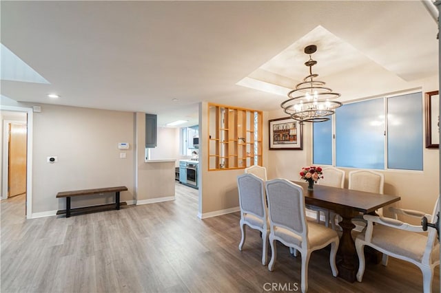 dining area with a raised ceiling, light wood-type flooring, and a chandelier