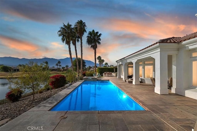 pool at dusk with a patio area and a mountain view