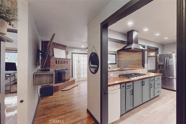 kitchen with a wood stove, wooden counters, wall chimney exhaust hood, gray cabinets, and stainless steel appliances