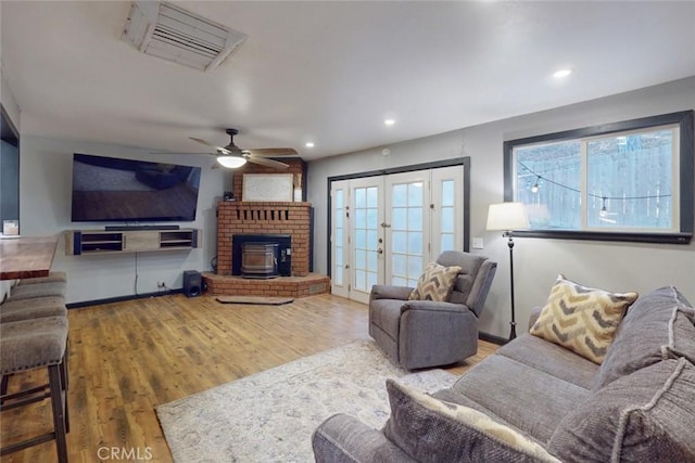 living room featuring hardwood / wood-style flooring, ceiling fan, a wood stove, and french doors