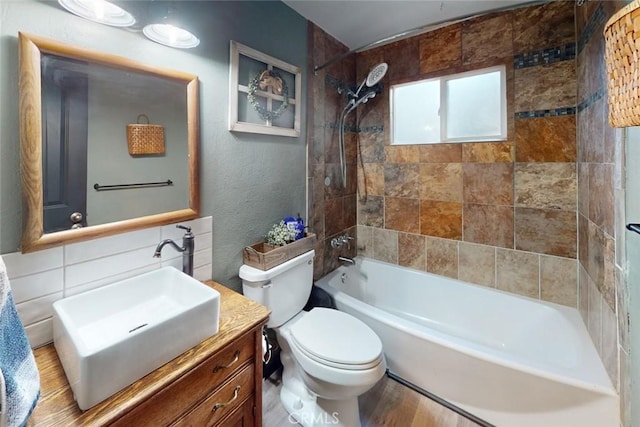 full bathroom with vanity, tiled shower / bath combo, hardwood / wood-style flooring, tile walls, and toilet