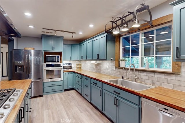 kitchen featuring wood counters, appliances with stainless steel finishes, light wood-type flooring, tasteful backsplash, and sink