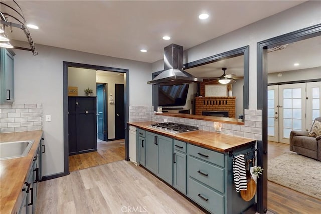 kitchen with beverage cooler, wooden counters, light hardwood / wood-style floors, stainless steel gas stovetop, and island range hood