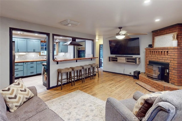 living room featuring light wood-type flooring, a wood stove, and ceiling fan