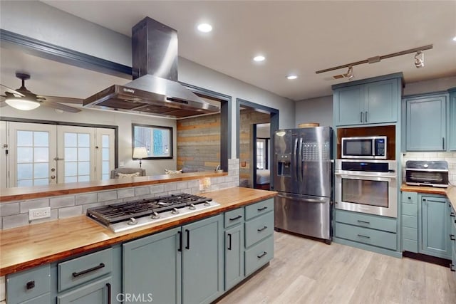 kitchen with backsplash, wall chimney range hood, stainless steel appliances, and wooden counters