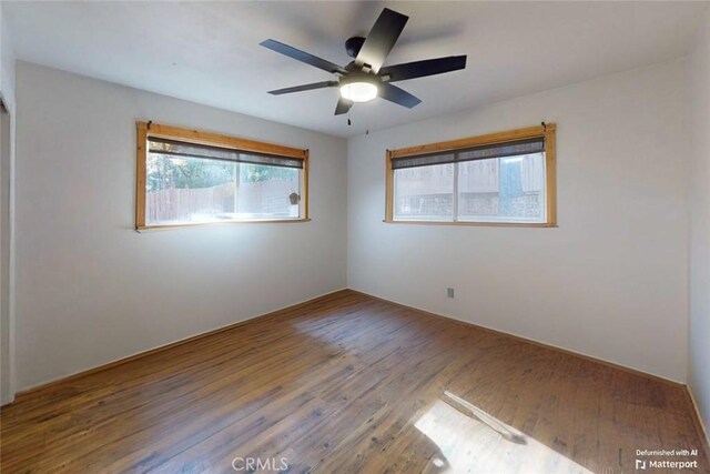 empty room with ceiling fan, a healthy amount of sunlight, and wood-type flooring