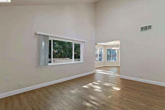 spare room with hardwood / wood-style floors, high vaulted ceiling, and an inviting chandelier