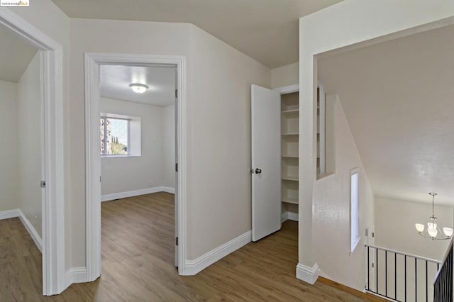 corridor featuring light wood-type flooring and an inviting chandelier