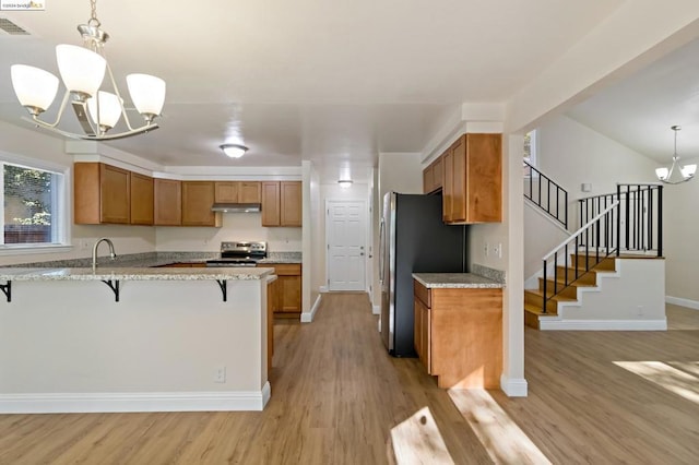 kitchen with pendant lighting, a breakfast bar, an inviting chandelier, light wood-type flooring, and appliances with stainless steel finishes