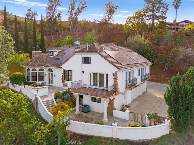 rear view of house featuring solar panels, cooling unit, a balcony, and french doors