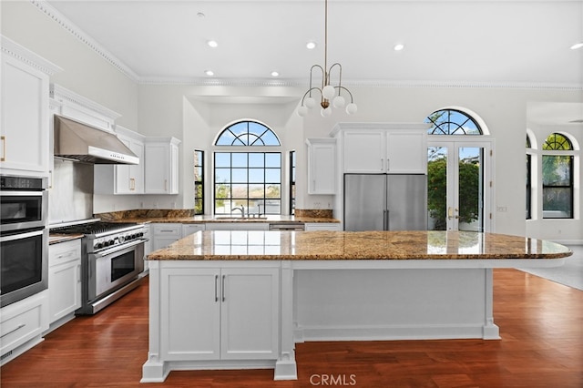 kitchen with light stone countertops, a center island, sink, wall chimney range hood, and appliances with stainless steel finishes