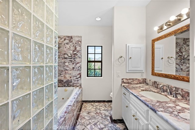 bathroom featuring vanity, a relaxing tiled tub, and toilet