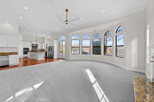 unfurnished living room featuring ceiling fan, sink, carpet, and ornamental molding