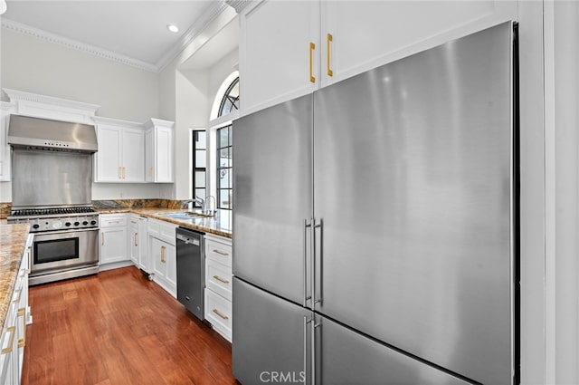 kitchen featuring white cabinetry, light stone counters, wall chimney range hood, and appliances with stainless steel finishes