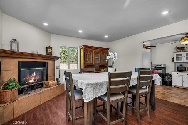 dining area with ceiling fan, dark hardwood / wood-style floors, and a tiled fireplace