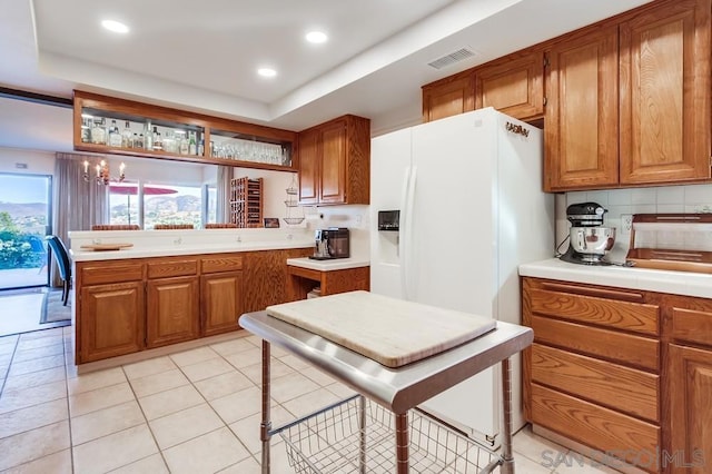 kitchen featuring tasteful backsplash, a tray ceiling, a notable chandelier, white fridge with ice dispenser, and light tile patterned flooring