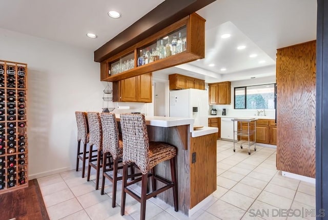 kitchen with a kitchen bar, kitchen peninsula, light tile patterned floors, and white appliances