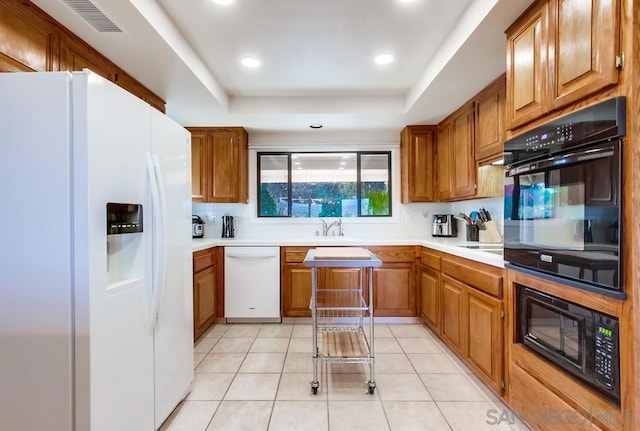 kitchen with a tray ceiling, light tile patterned flooring, and white appliances