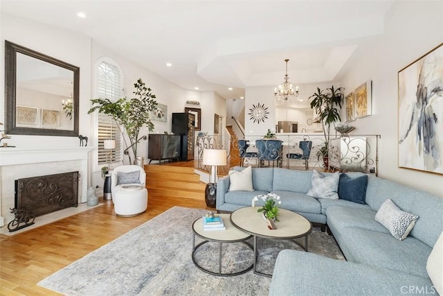 living room with a tiled fireplace, hardwood / wood-style floors, a tray ceiling, and a notable chandelier