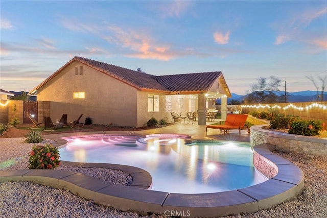 pool at dusk featuring an in ground hot tub, a mountain view, and a patio