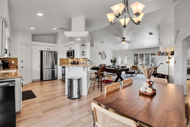 dining space featuring ceiling fan with notable chandelier, light hardwood / wood-style floors, sink, and vaulted ceiling