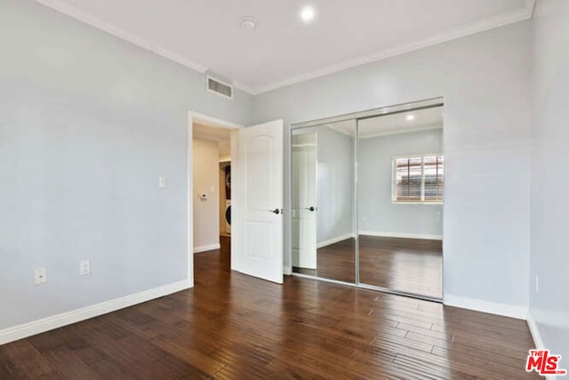 unfurnished bedroom with dark hardwood / wood-style flooring, ornamental molding, and a closet