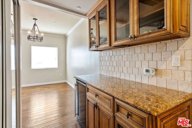 kitchen with pendant lighting, decorative backsplash, light stone counters, crown molding, and light hardwood / wood-style flooring