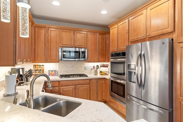 kitchen featuring light stone counters, sink, decorative light fixtures, and appliances with stainless steel finishes