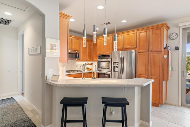 kitchen with kitchen peninsula, appliances with stainless steel finishes, a kitchen bar, pendant lighting, and light tile patterned flooring