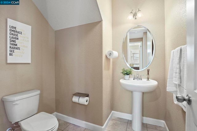 bathroom with toilet, tile patterned flooring, vaulted ceiling, and sink