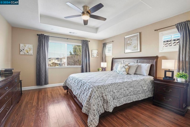 bedroom featuring ceiling fan, dark wood-type flooring, a tray ceiling, and multiple windows