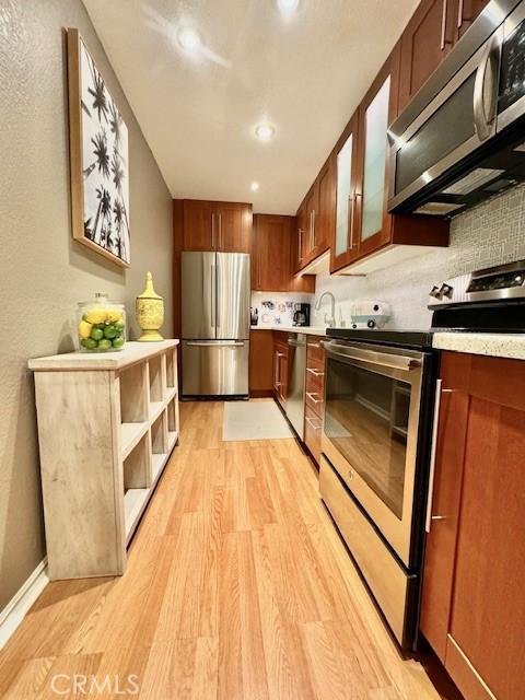 kitchen with glass insert cabinets, light wood-type flooring, light countertops, decorative backsplash, and appliances with stainless steel finishes